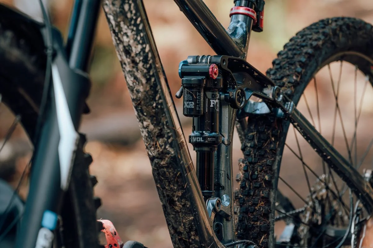 Detailed view of a mountain bike with muddy suspension and frame in a natural outdoor setting.