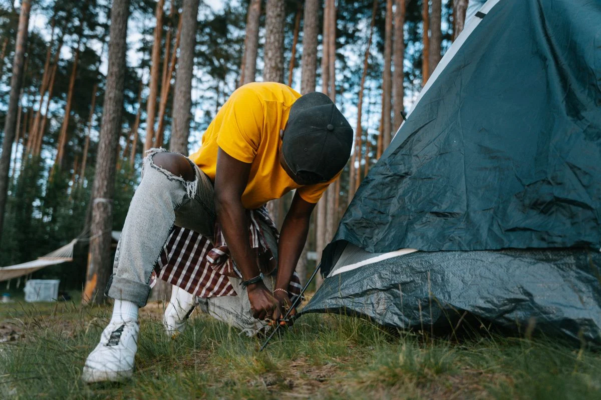 Adult man in casual attire setting up a tent in a forest campsite, embodying adventure and outdoor leisure.