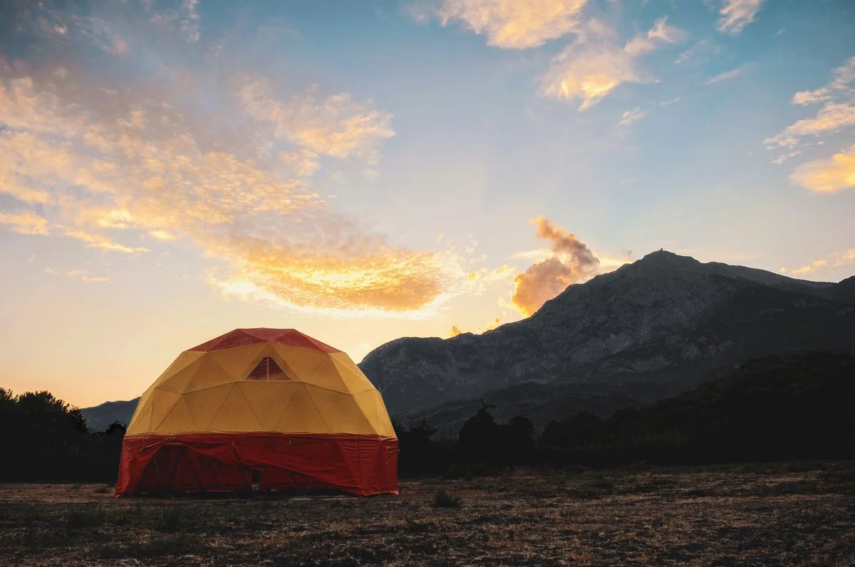 Geodesic tent under a vibrant sunset with mountains in the background.