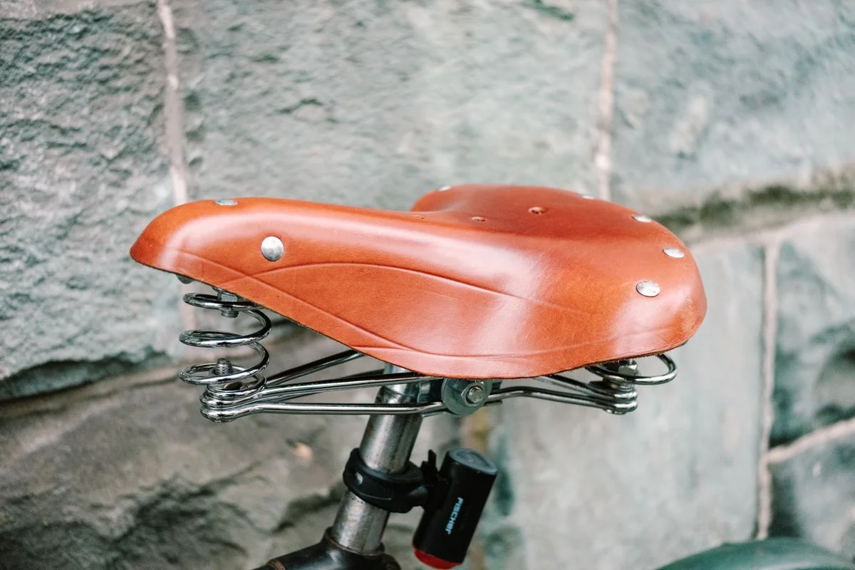 Close-up of a vintage leather bicycle seat with metal springs against a stone wall.