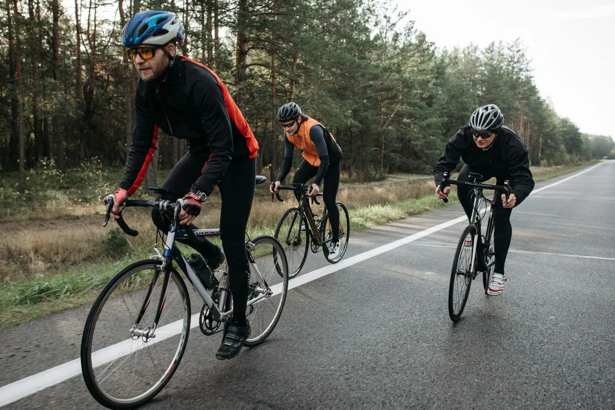 Three cyclists in activewear enjoy a ride along a scenic forest road at daytime.