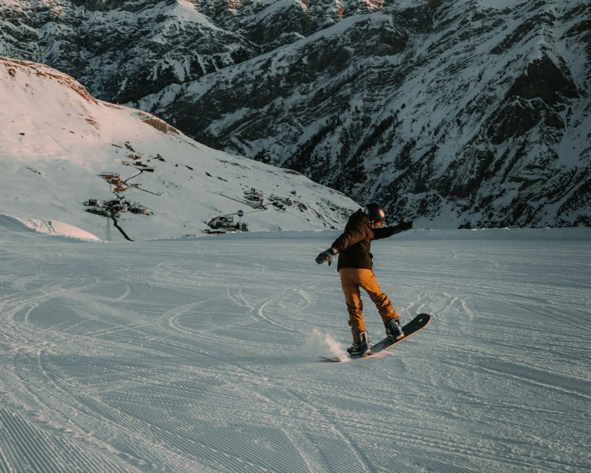 A snowboarder gracefully gliding down a snowy mountain slope during a winter sunset.