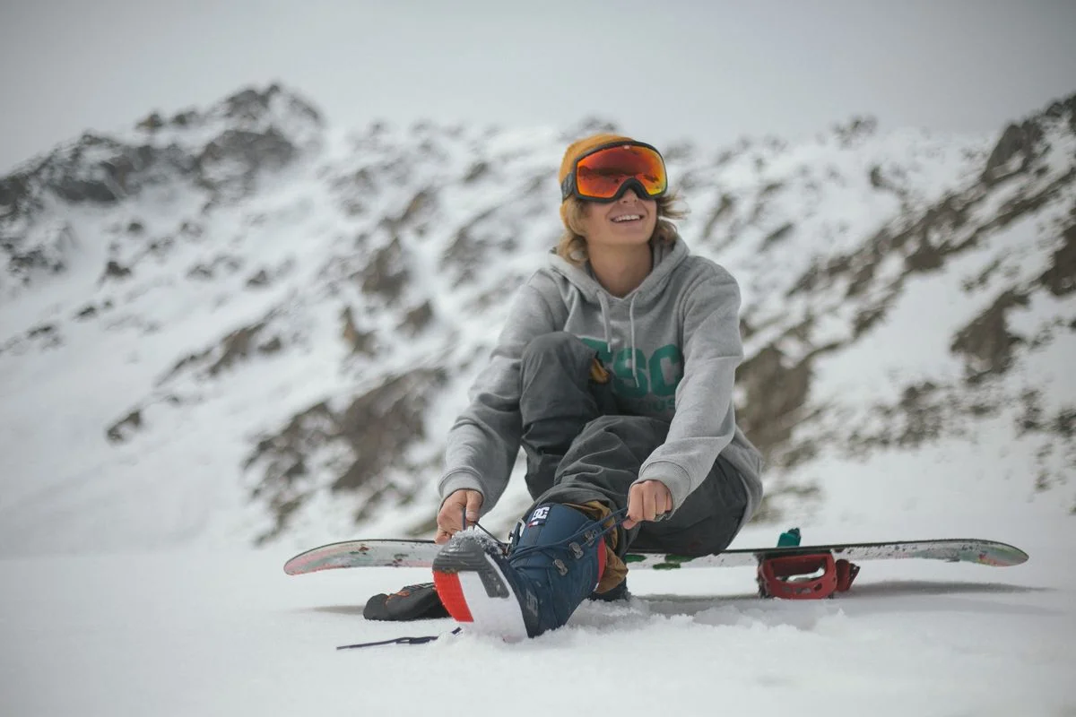 Woman snowboarder tying boots, enjoying a winter day in snowy mountains.