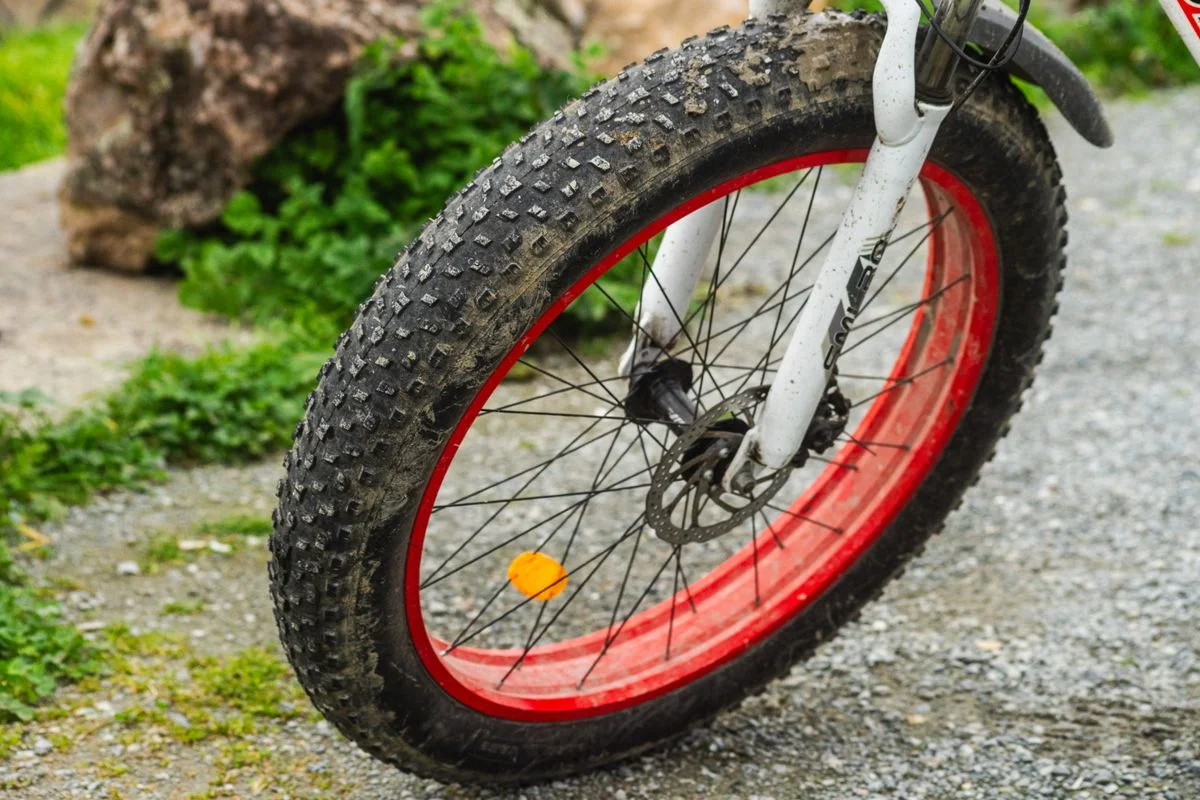 Close-up image capturing a dirty bicycle tire with red rim on a gravel path.