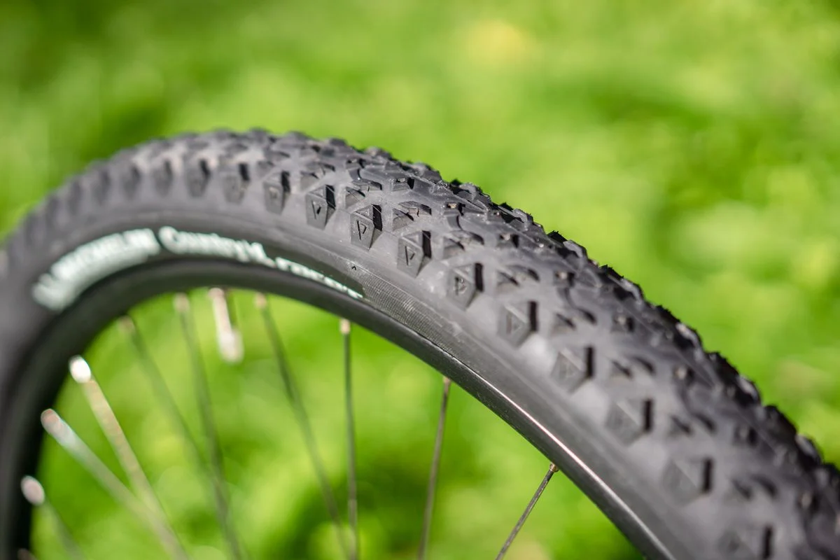 Detailed view of a mountain bike tire showing tread patterns against a blurred background.